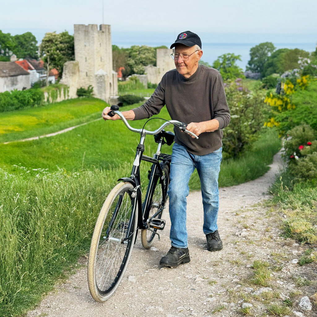 Äldre man tar sin cykel uppför en backe. Bertil Annas fotograferat av Rickard Hamrén.